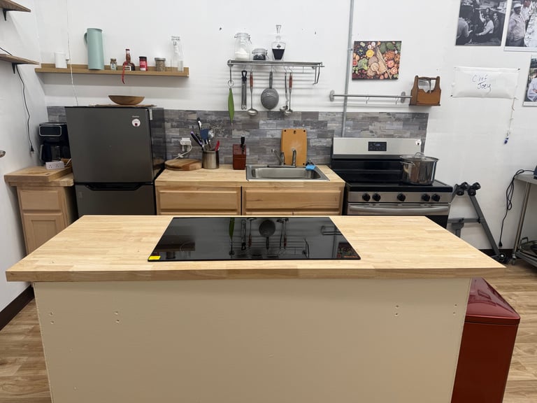 Modern kitchen with white island countertop, wooden cabinets, black appliances, and open shelving with cooking utensils and décor.
